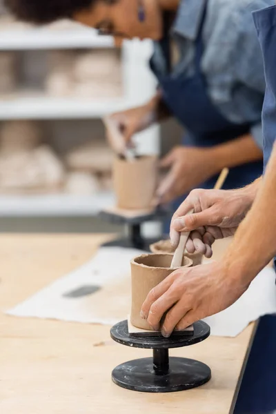 Uomo formando tazza di argilla vicino offuscata fidanzata afro-americana in laboratorio di ceramica — Foto stock