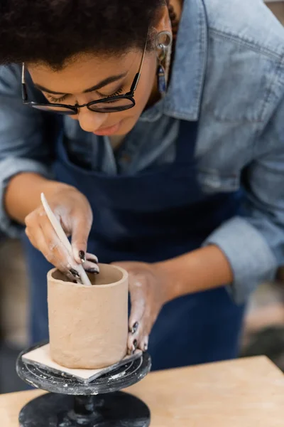 African american craftswoman in eyeglasses forming clay cup in workshop — Stock Photo