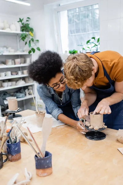 African american craftswoman helping man making clay cup in pottery studio — Stock Photo