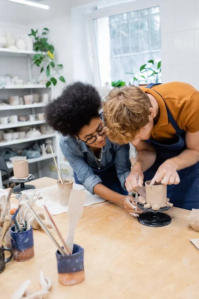 Artigiana afroamericana aiutare l'uomo a fare tazza di argilla in studio di ceramica — Foto stock