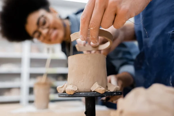 Homme tenant de l'argile près de la sculpture et professeur afro-américain flou dans un atelier de poterie — Photo de stock