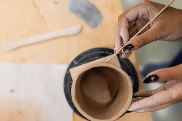 Blick von oben auf afrikanisch-amerikanische Kunsthandwerkerin, die im Töpferatelier Keramikprodukt mit Holzstab herstellt — Stockfoto