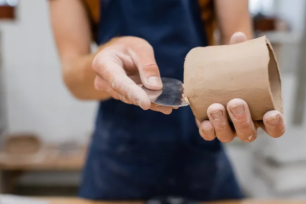 Cropped view of sculptor forming clay product with steel scraper in pottery workshop — Stock Photo