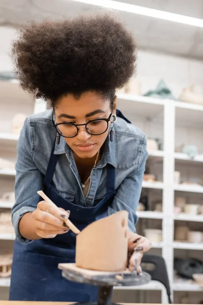 African american artisan in eyeglasses and apron making clay sculpture in workshop — Stock Photo