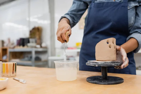 Vue recadrée d'un sculpteur afro-américain tenant une éponge avec de l'eau près d'une sculpture en argile dans un atelier — Photo de stock