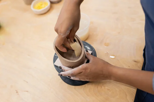 Обрезанный вид на африканскую американскую ремесленницу, формирующую глиняный продукт с губкой — стоковое фото