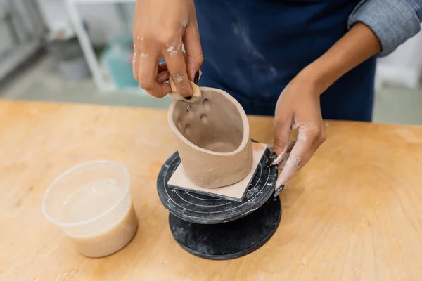 Vista recortada de la artesana afroamericana formando escultura de arcilla con esponja en taller de cerámica — Stock Photo