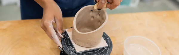 Vue recadrée du maître afro-américain formant de l'argile avec éponge en atelier de poterie, bannière — Photo de stock