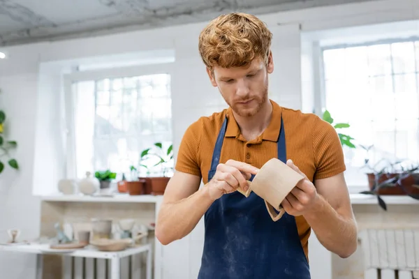 Redhead artisan dans tablier fabrication tasse en céramique en atelier de poterie — Photo de stock