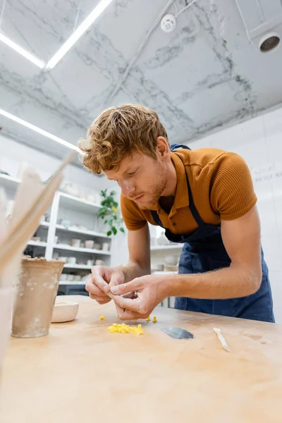 Young artisan in apron holding pottery tools in workshop — Stock Photo