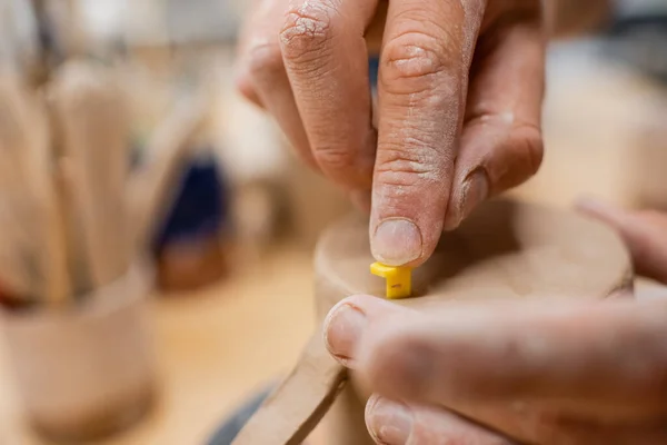 Cropped view of artisan pressing tool in clay in pottery workshop — Stock Photo