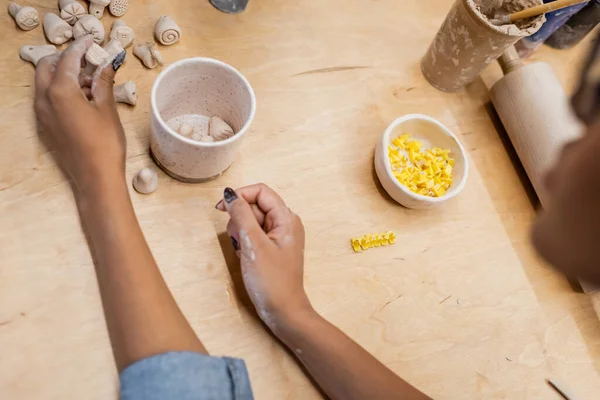 Vue recadrée du maître afro-américain tenant une sculpture en argile près de la table dans un atelier de poterie — Photo de stock