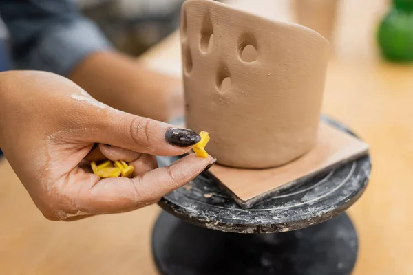 Ausgeschnittene Ansicht einer afrikanisch-amerikanischen Kunsthandwerkerin, die Werkzeuge in der Nähe von Tonskulpturen in der Werkstatt hält — Stockfoto