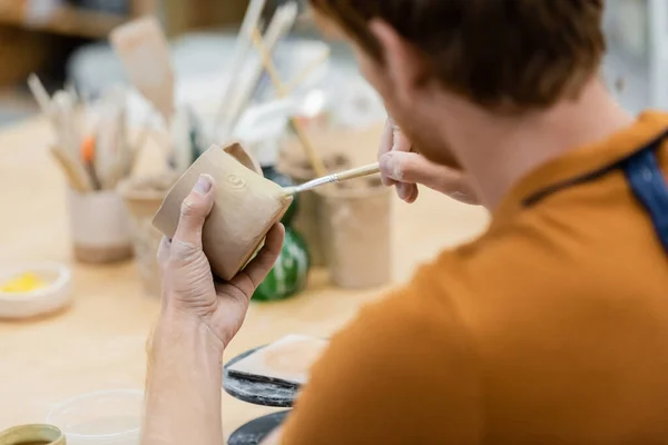 Young craftsman painting on clay cup in pottery workshop — Stock Photo