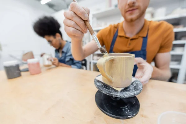 Homem borrado pintando na xícara de cerâmica perto da namorada americana africana no estúdio de cerâmica — Fotografia de Stock