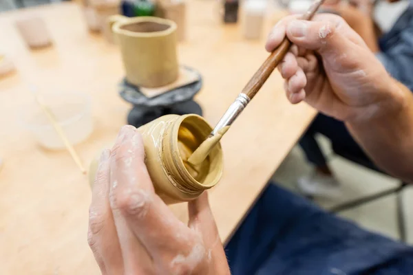 Vue recadrée d'un homme tenant un pinceau et de la peinture dans un atelier de poterie — Photo de stock