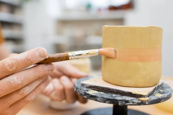 Обрезанный вид малярной живописи на глиняный продукт в мастерской — стоковое фото