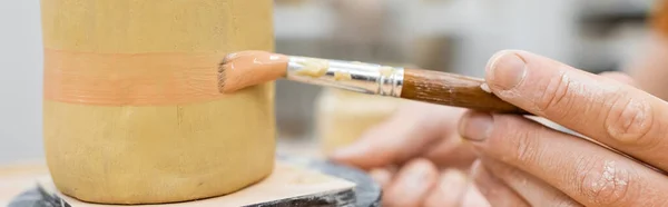 Cropped view of craftsman painting on ceramic sculpture in workshop, banner — Stock Photo