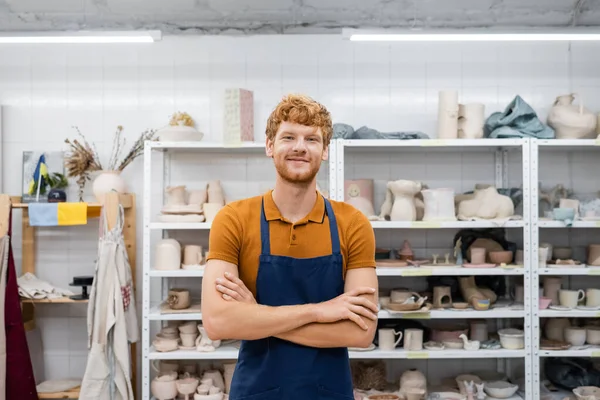 Sorrindo artesão ruiva olhando para a câmera na oficina de cerâmica — Fotografia de Stock