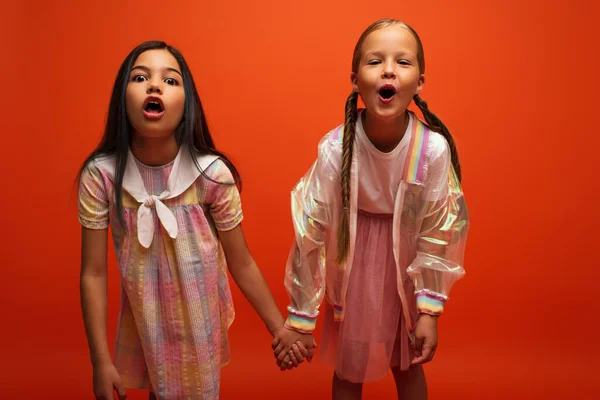 Lustige Mädchen mit offenen Mündern, die Hände halten und in die Kamera grimmen, isoliert auf orange — Stockfoto