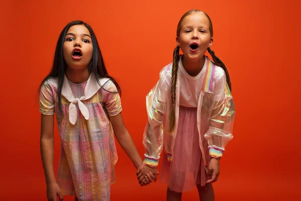 Funny girls with open mouths holding hands and grimacing at camera isolated on orange — Stock Photo