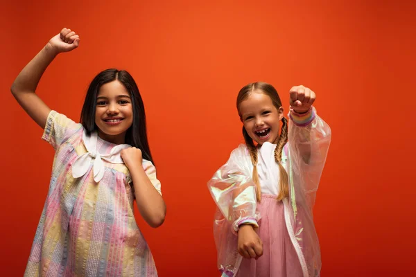 Веселые девушки, смотрящие в камеру и показывающие сжатые кулаки, наслаждаясь изолированным апельсином — стоковое фото