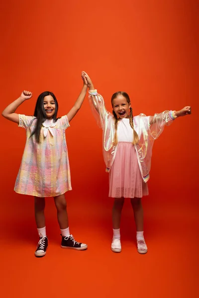 Comprimento total de meninas animadas dando alta cinco e mostrando gesto de vitória no fundo laranja — Fotografia de Stock