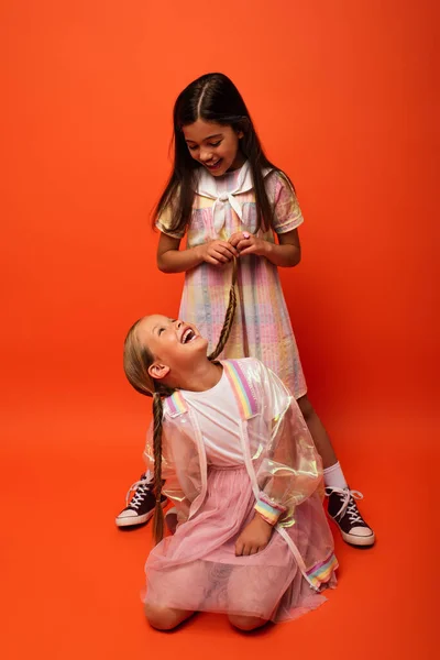 Brünettes Mädchen hält Zopf von fröhlichen Freund sitzt auf orangefarbenem Hintergrund — Stockfoto