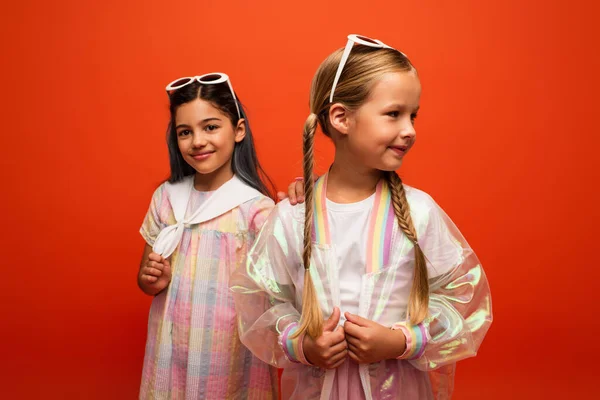 Smiling girl in dress touching shoulder of friend with pigtails isolated on orange — Stock Photo