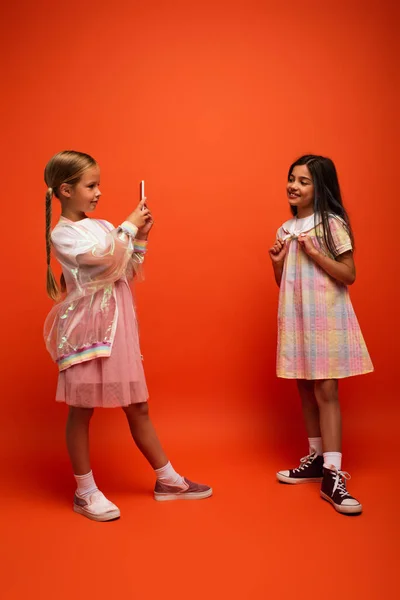 Volle Länge des Kindes in Regenjacke Aufnahme Foto von lächelnden brünetten Mädchen in Kleid auf orangefarbenem Hintergrund — Stockfoto