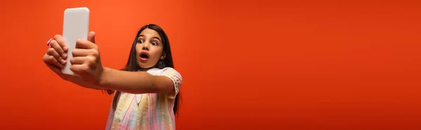 Menina assustada com a boca aberta tomando selfie no celular isolado em laranja, banner — Fotografia de Stock