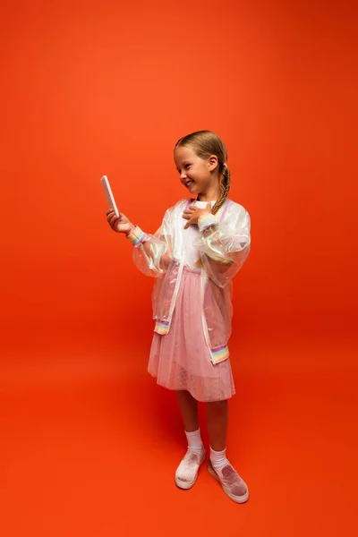 Comprimento total da menina feliz tocando no peito durante a chamada de vídeo no celular no fundo laranja — Fotografia de Stock