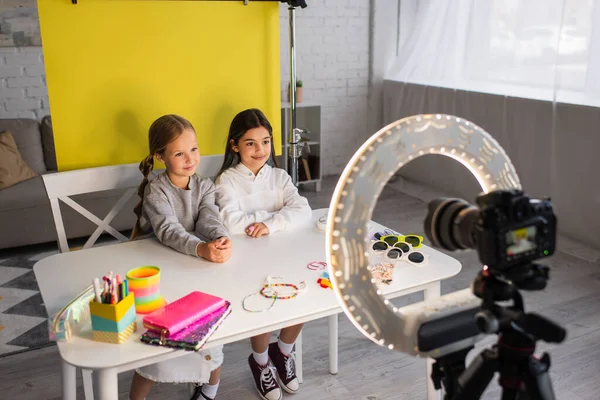 Video blogger sorridenti che guardano la fotocamera digitale vicino agli occhiali da sole e ai diversi accessori sul tavolo — Foto stock