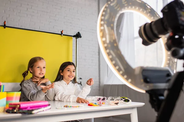 Preteen bloggers talking near different accessories on table near digital camera with ring light on blurred foreground — Stock Photo