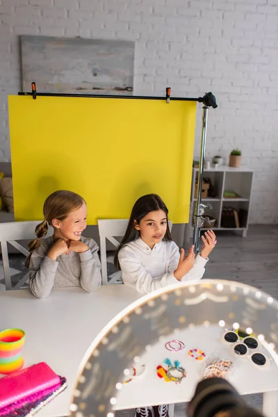 Brunette girl talking near cheerful blogger on yellow background in front of blurred circle light — Stock Photo