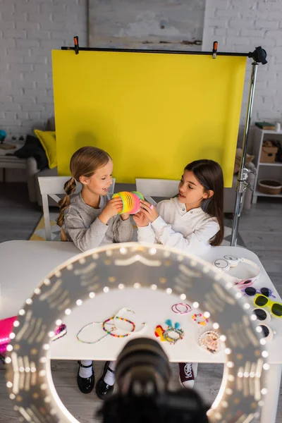 Pré-adolescentes blogueiros mostrando brinquedo espiral perto de câmera digital borrada em círculo de luz no fundo amarelo em casa — Fotografia de Stock