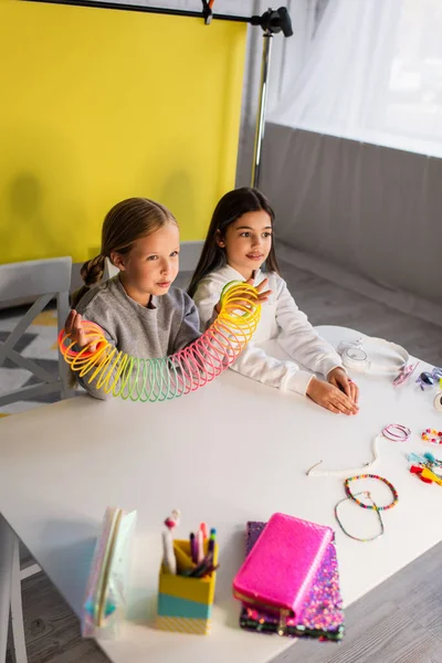 Blogger mostrando brinquedo espiral perto de amigo e acessórios diferentes na mesa — Fotografia de Stock