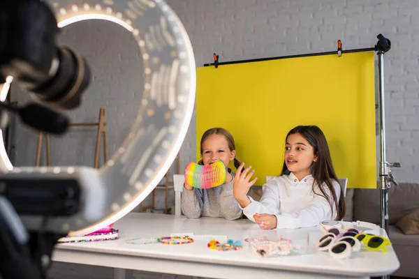 Preteen video blogger parlando vicino amico in possesso di spirale giocattolo davanti alla fotocamera digitale su sfondo giallo a casa — Foto stock