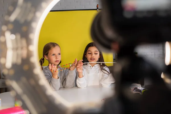 Câmera digital borrada e lâmpada de círculo perto de blogueiros pré-adolescentes mostrando contas no fundo amarelo — Fotografia de Stock
