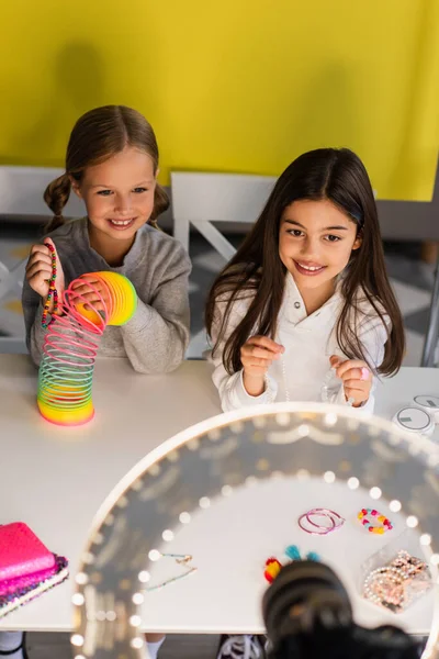 Happy blogger talking near friend with spiral toy and circle lamp on blurred foreground — Stock Photo