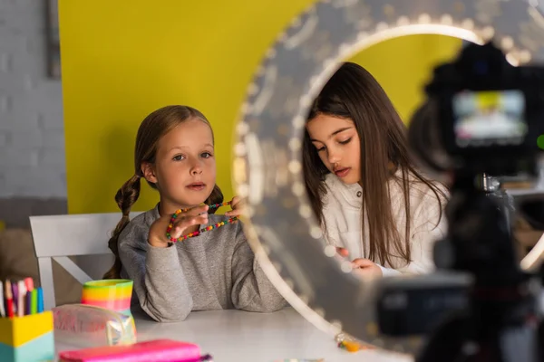 Video blogger che mostra perline vicino amico e fotocamera digitale con lampada cerchio in primo piano sfocato — Foto stock