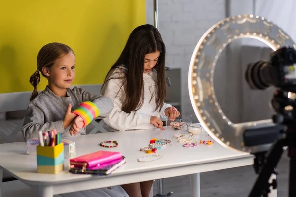 Preteen bloggers with spiral toy and beaded bracelets near digital camera with ring light on blurred foreground — Stock Photo