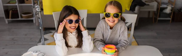 Happy video bloggers in trendy sunglasses near spiral toy and wireless headphones, banner — Stock Photo