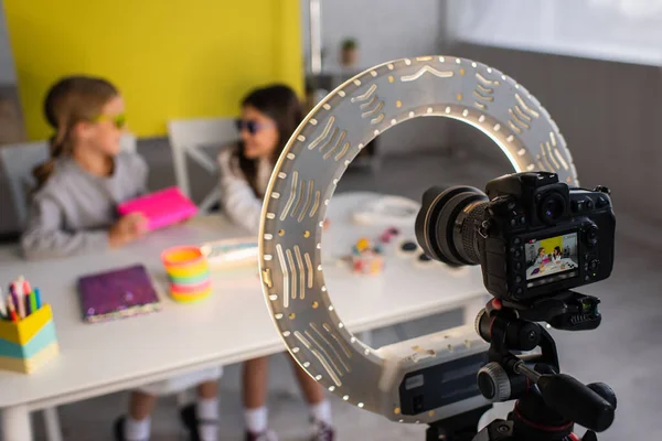 Selective focus of digital camera with ring light near blurred girls recording video blog at home — Stock Photo