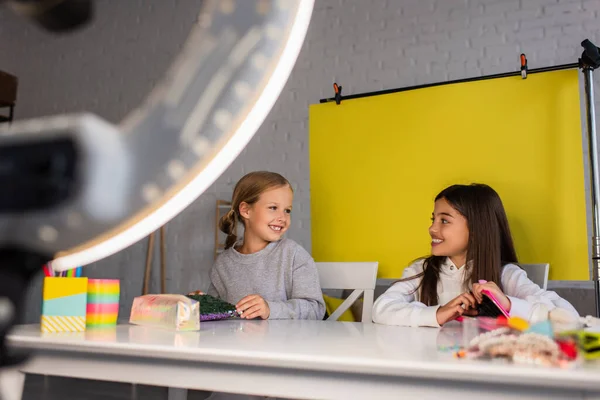 Happy bloggers smiling at each other on yellow background near blurred ring light at home — Stock Photo