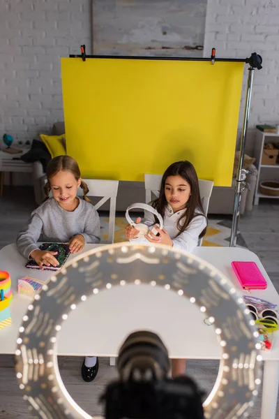 Preteen bloggers with wireless headphones and notebook near blurred circle lamp with digital camera — Stock Photo