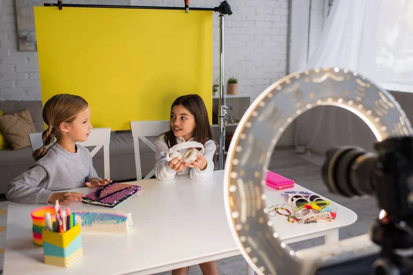 Preteen Girls mit Notizbuch und drahtlosem Kopfhörer sprechen auf gelbem Hintergrund vor verschwommener Digitalkamera — Stockfoto