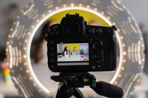 Selective focus of circle lamp and digital camera with screen showing girls recording video blog — Stock Photo