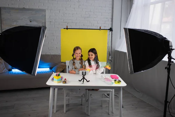 Smiling video bloggers showing spiral toy in front of cellphone on phone holder near yellow background at home — Stock Photo