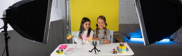 Cheerful girls showing spiral toy while recording video blog on yellow background at home, banner — Stock Photo